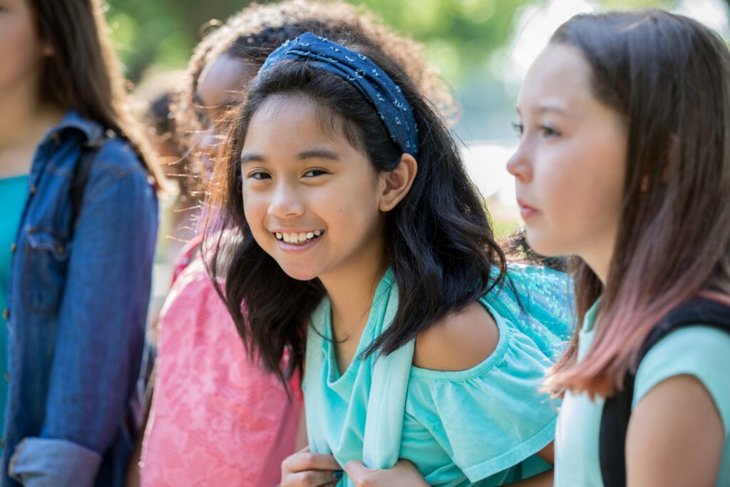 A young girl smiles at the camera as she stands with a group of other girls, ready to move to their next class.