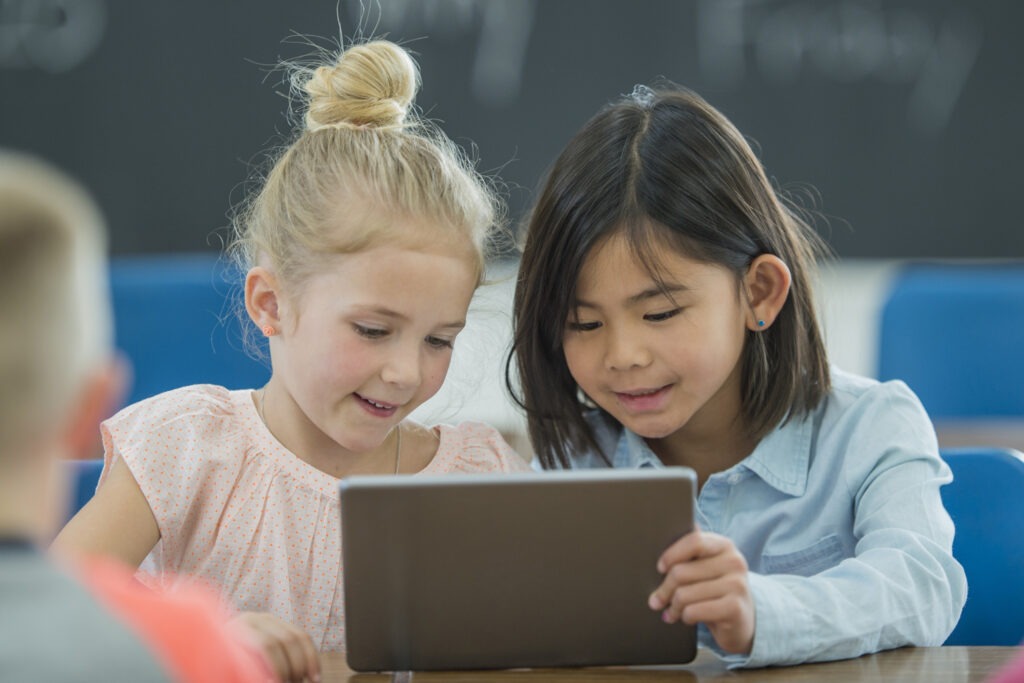 Two school-age girls share a learning tablet.