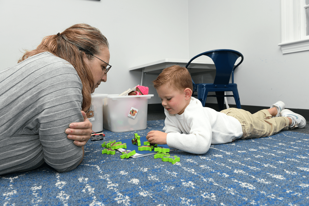 A speech therapist plays with a student on the floor, helping him develop speech skills.