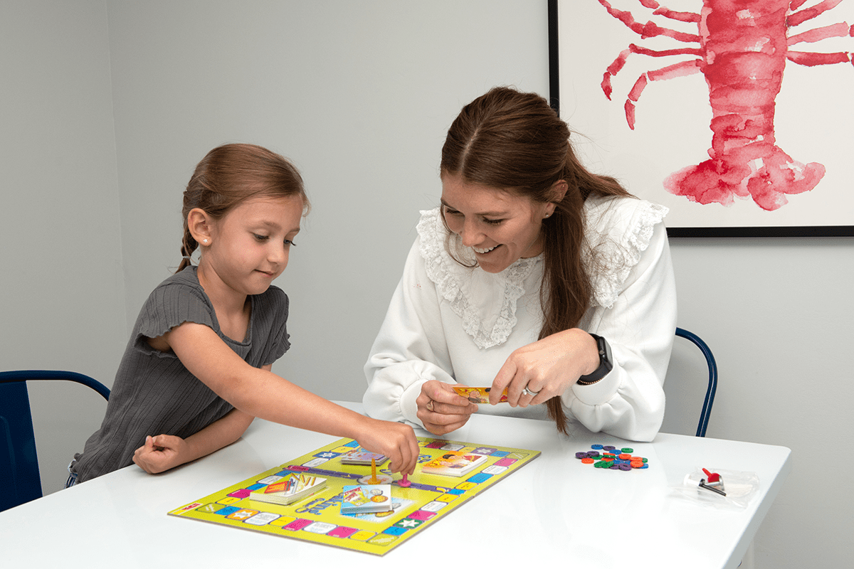 A teacher and student play an educational board game together, blending learning with recreational play.