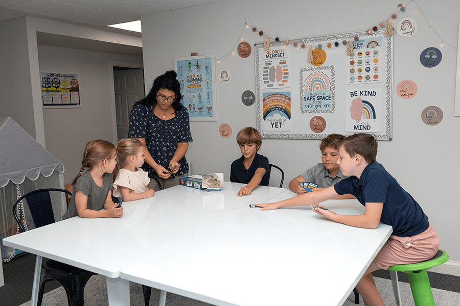 A teacher shows one of her school-age pupils how to play an educational game with a group of her peers.